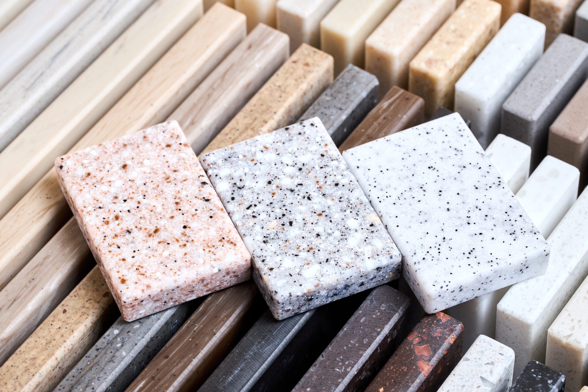 Porcelain three stoneware square samples laid on kitchen countertop examples of future kitchen fasade exterior. Samples slabs of natural granite marble quartz for stone countertops close up.